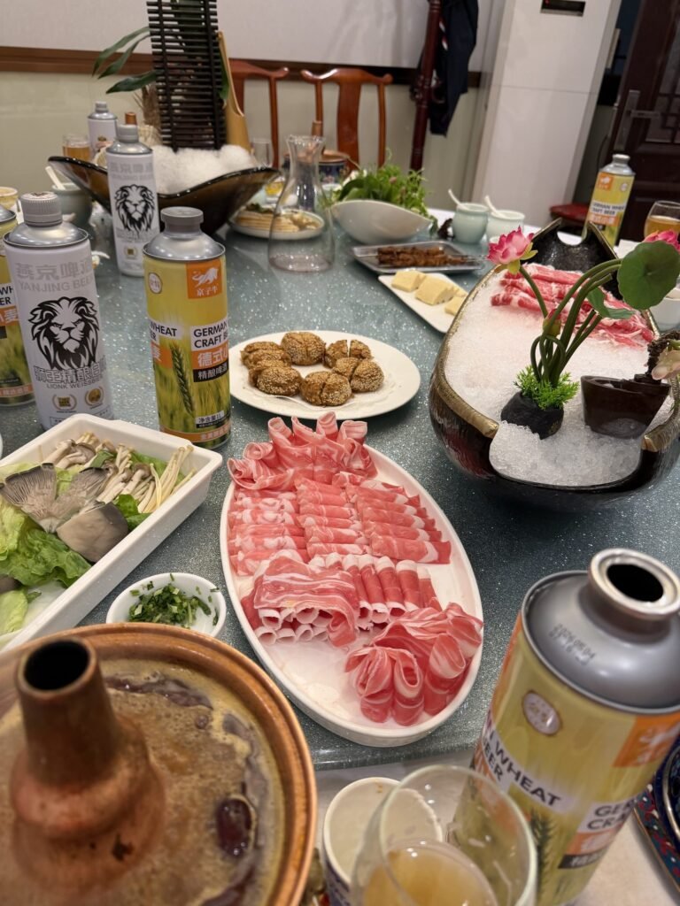 A Beijing-style hotpot dinner: a copper chimney pot with platters of thinly sliced lamb and beef, mushrooms and greens, sesame cakes and cans of Yanjing beer