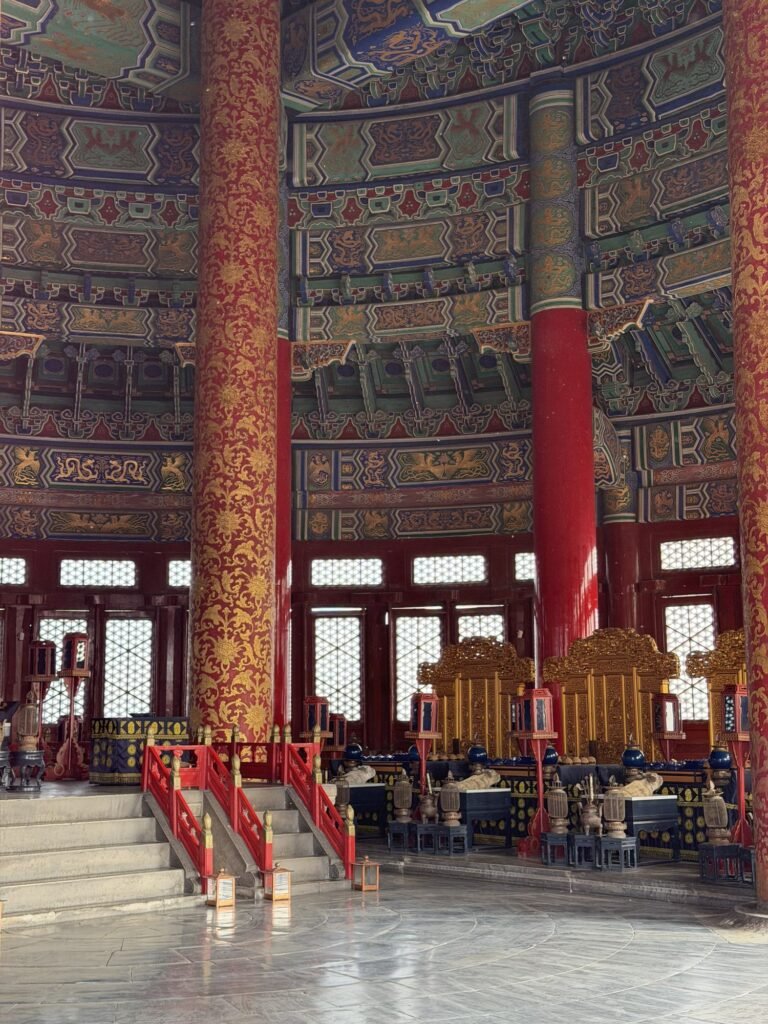 Inside the Hall of Prayer for Good Harvests: tall red columns painted with gold patterns, a red-railed stairway and an ornate gilded altar area under a painted ceiling