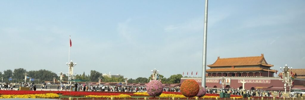 Tiananmen Gate with its orange-tiled roof beside Tiananmen Square, with red and yellow flower beds and large flower spheres along the avenue
